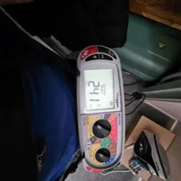 Miernik Megger MFT1741+ wyświetla wynik pomiaru 50.0 Hz oraz 241 V~, leżący obok żelazka na podłodze w trakcie pomiarów elektrycznych.