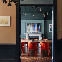 TK&ELECTRICS - Stylowe wykończenie wnętrza w Skokach: widok na pokój z pomarańczowymi krzesłami i stołem do ping-ponga, oryginalna podłoga i oświetlenie.