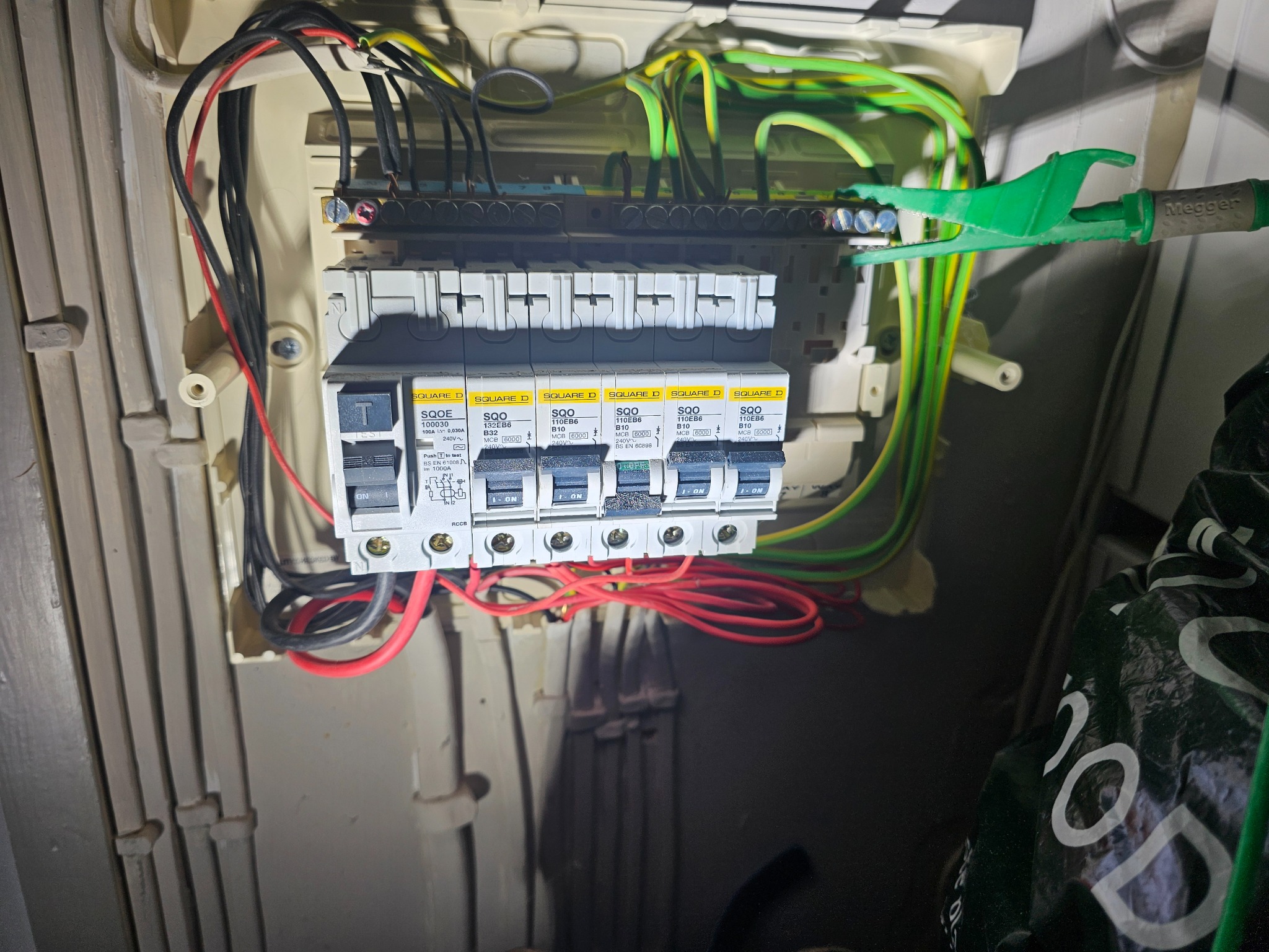 Rozdzielnica elektryczna z zamontowanymi bezpiecznikami, okablowaniem i zielonymi klemami pomiarowymi Megger, widoczna wnęka z przewodami.