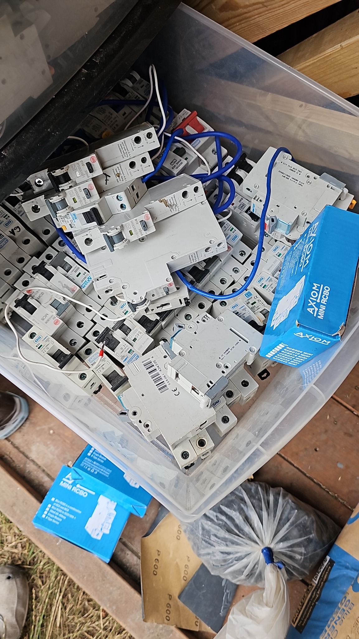 Kosz z wyłącznikami nadprądowymi, przewody i pudełka Axiom Mini RCBO. Elementy instalacji elektrycznej w nieładzie, widok z góry, na drewnianym podłożu.