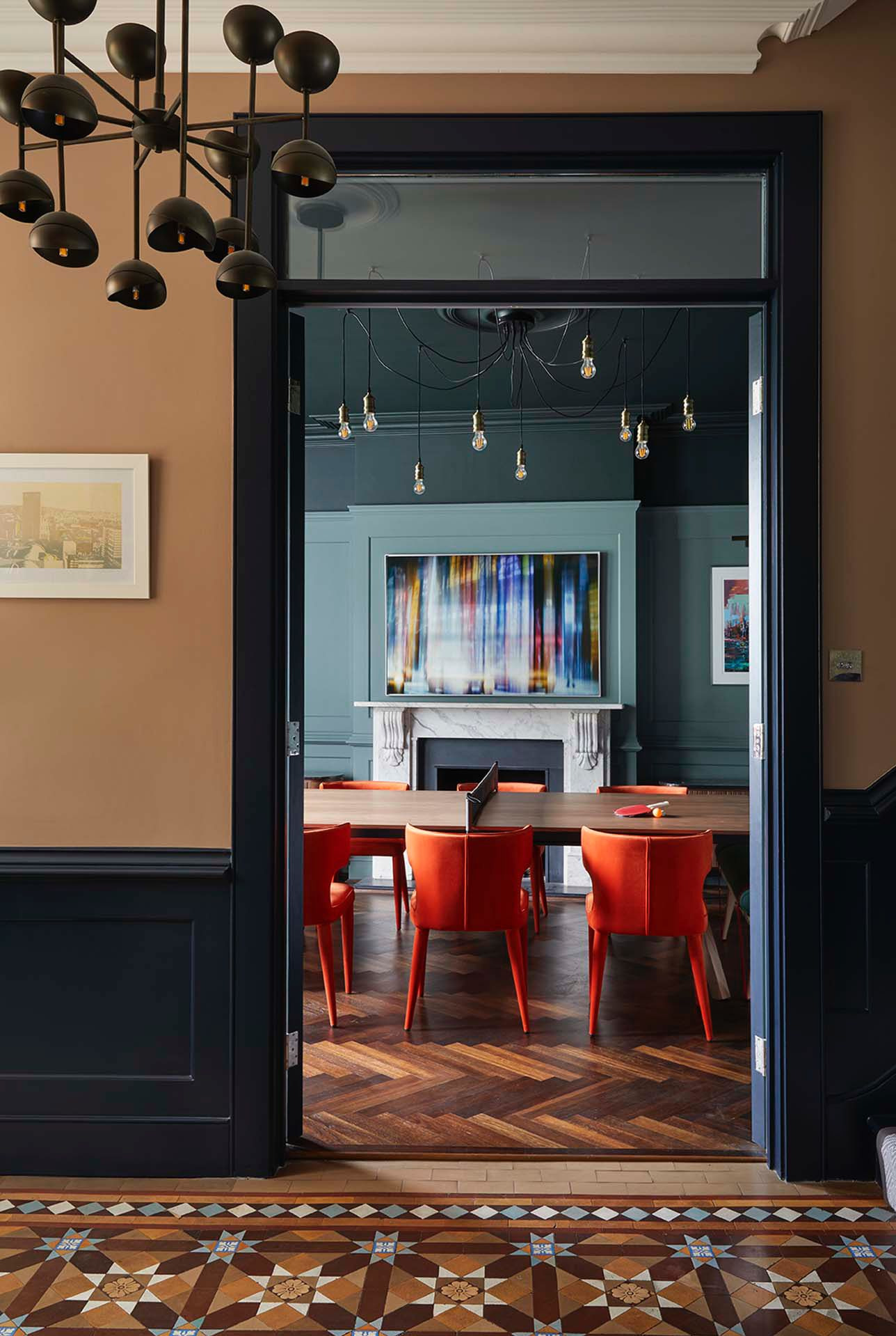 Stylowe wykończenie wnętrza w Skokach: widok na pokój z pomarańczowymi krzesłami i stołem do ping-ponga, oryginalna podłoga i oświetlenie.