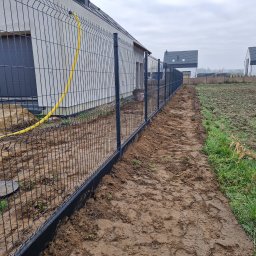 PRO FENCE KRZYSZTOF KOŁTYŚ - Montaż ogrodzenia panelowego z podmurówką betonową, widoczny żółty przewód gazowy przy ścianie budynku, świeżo przekopana ziemia wzdłuż ogrodzenia.