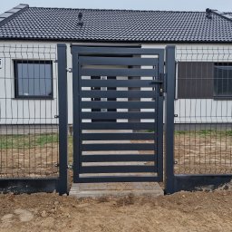 PRO FENCE KRZYSZTOF KOŁTYŚ - Nowoczesna brama wjazdowa z poziomymi panelami w kolorze antracytowym, zamontowana w ogrodzeniu z siatki, na tle białego domu z ciemną dachówką.