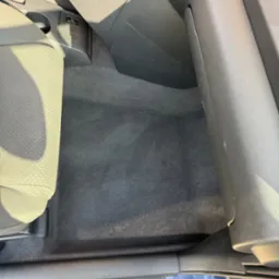 Wnętrze samochodu z wyczyszczoną tapicerką podłogową, widoczny fragment fotela, konsola środkowa i próg drzwi.