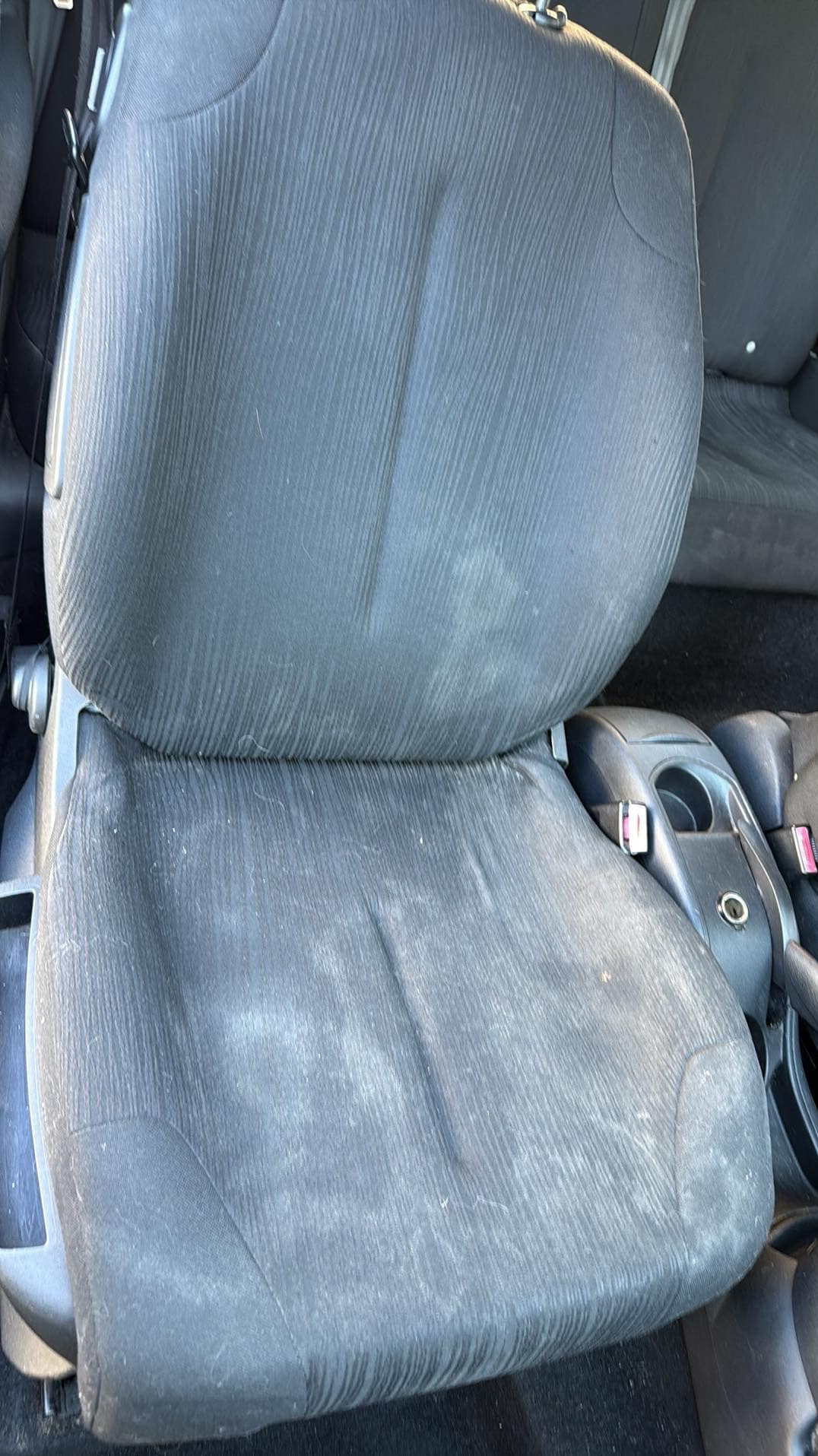 Brudne, tekstylne siedzenie samochodowe w odcieniach szarości, widoczne plamy i drobne zabrudzenia na powierzchni materiału.