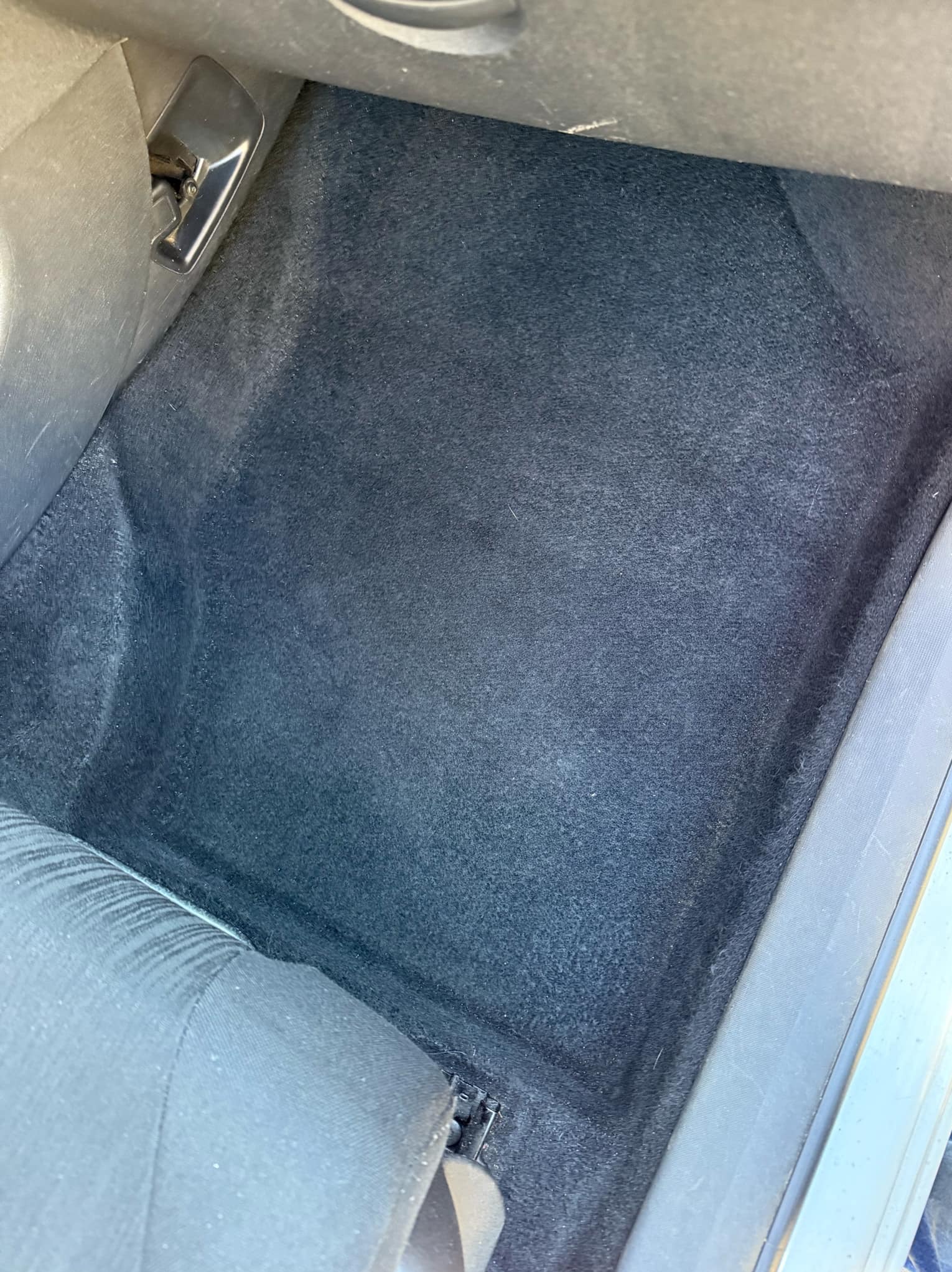 Wnętrze samochodu, widok na czarną tapicerkę podłogi za siedzeniem pasażera, widoczny fragment fotela i element mocujący.