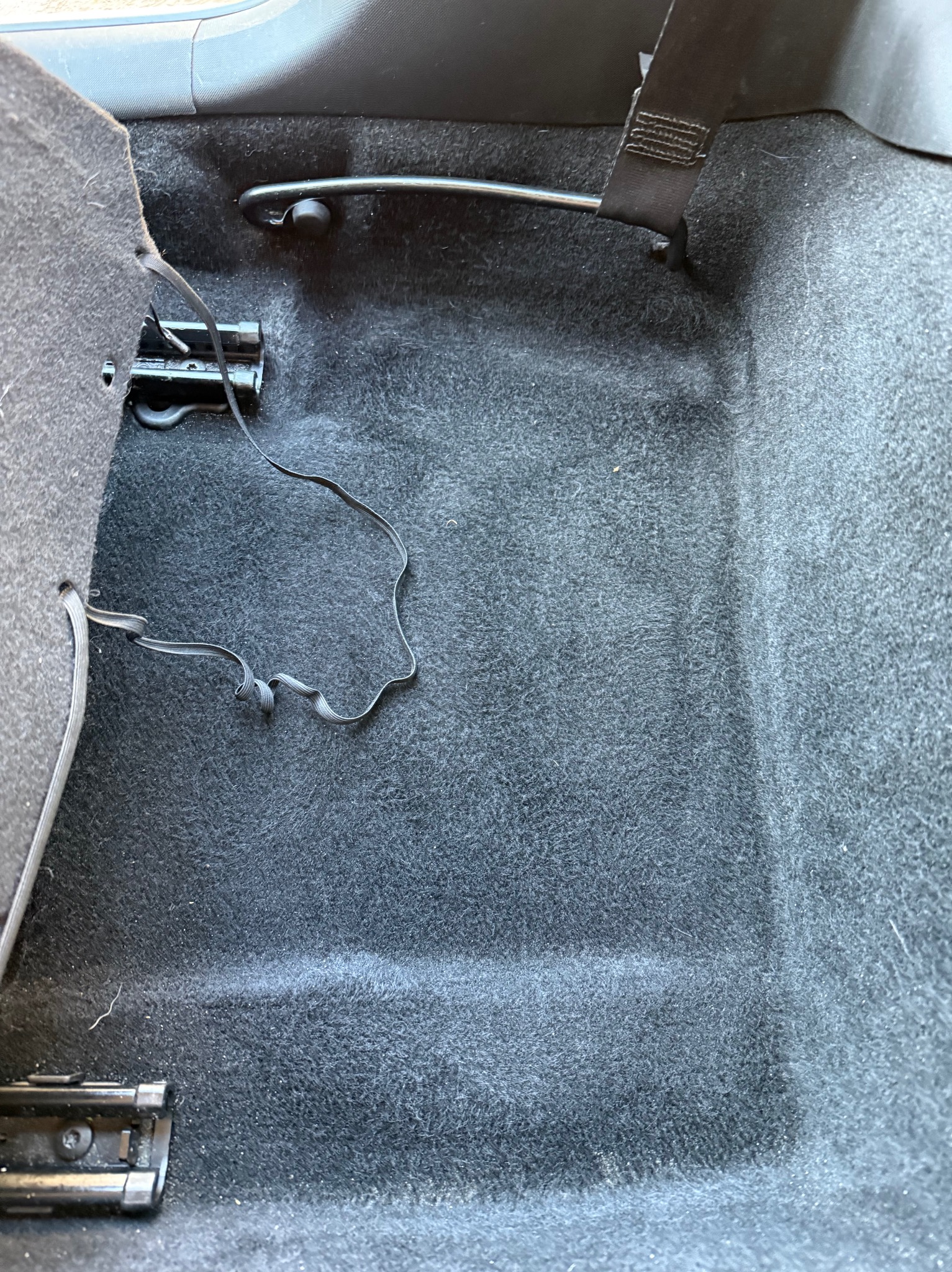 Ciemnoszara tapicerka podłogowa samochodu z widocznymi elementami mocującymi siedzenia i pasy bezpieczeństwa.