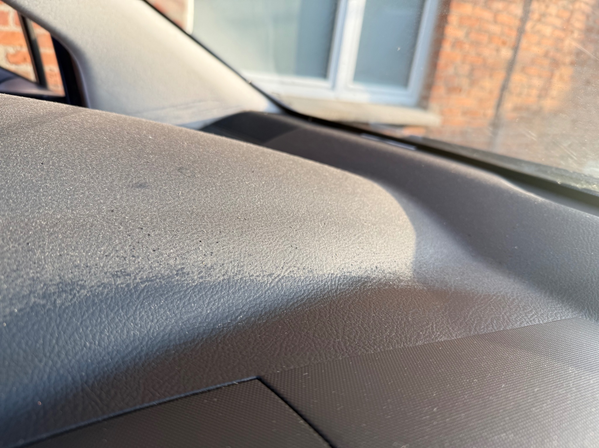 Zakurzona deska rozdzielcza samochodu w zbliżeniu, widoczne drobinki brudu i struktura materiału.