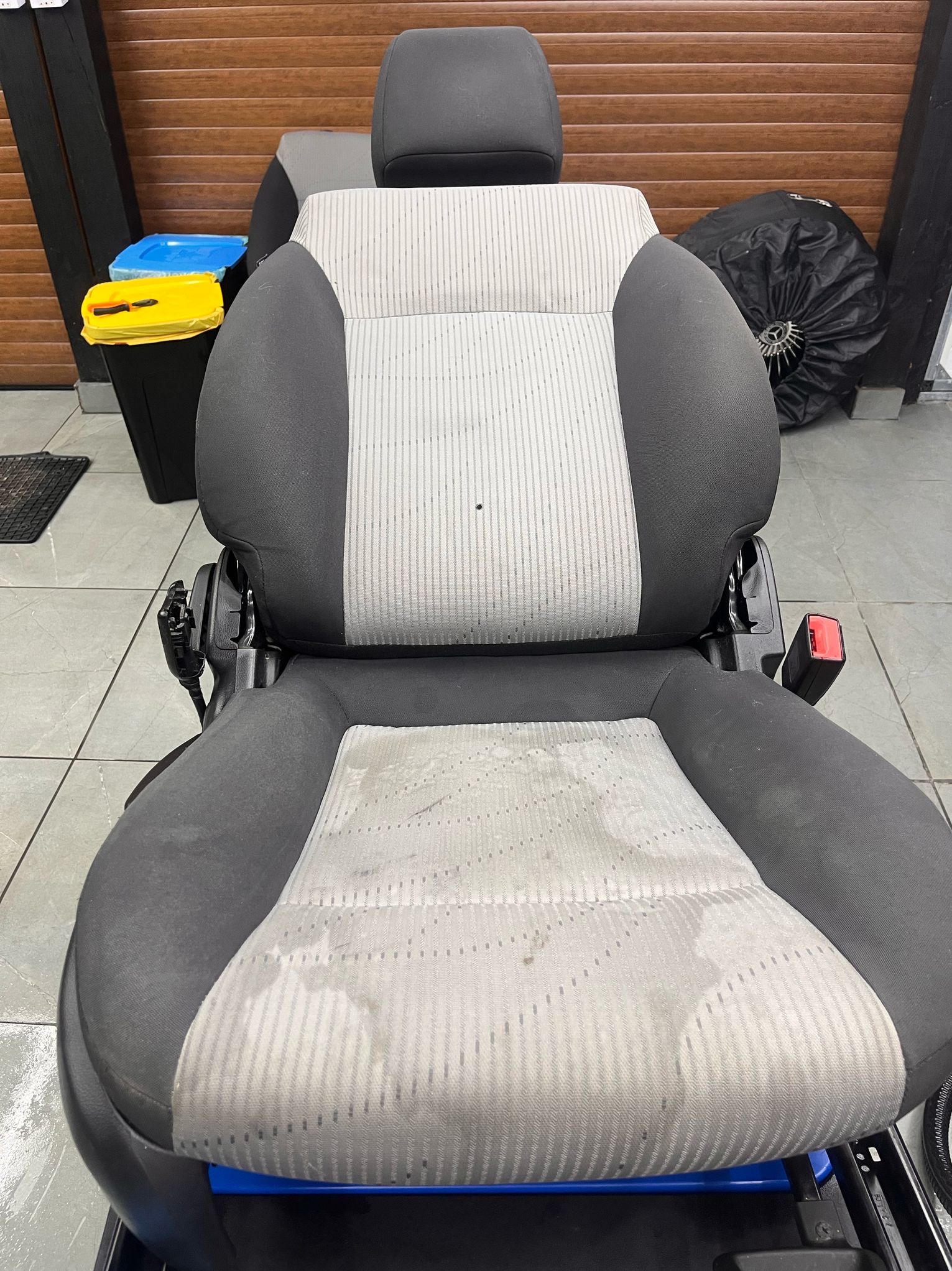 Tapicerowane fotel samochodowy z wyraźnymi plamami na siedzisku, przed praniem, widoczne szare i białe pasy na materiale.