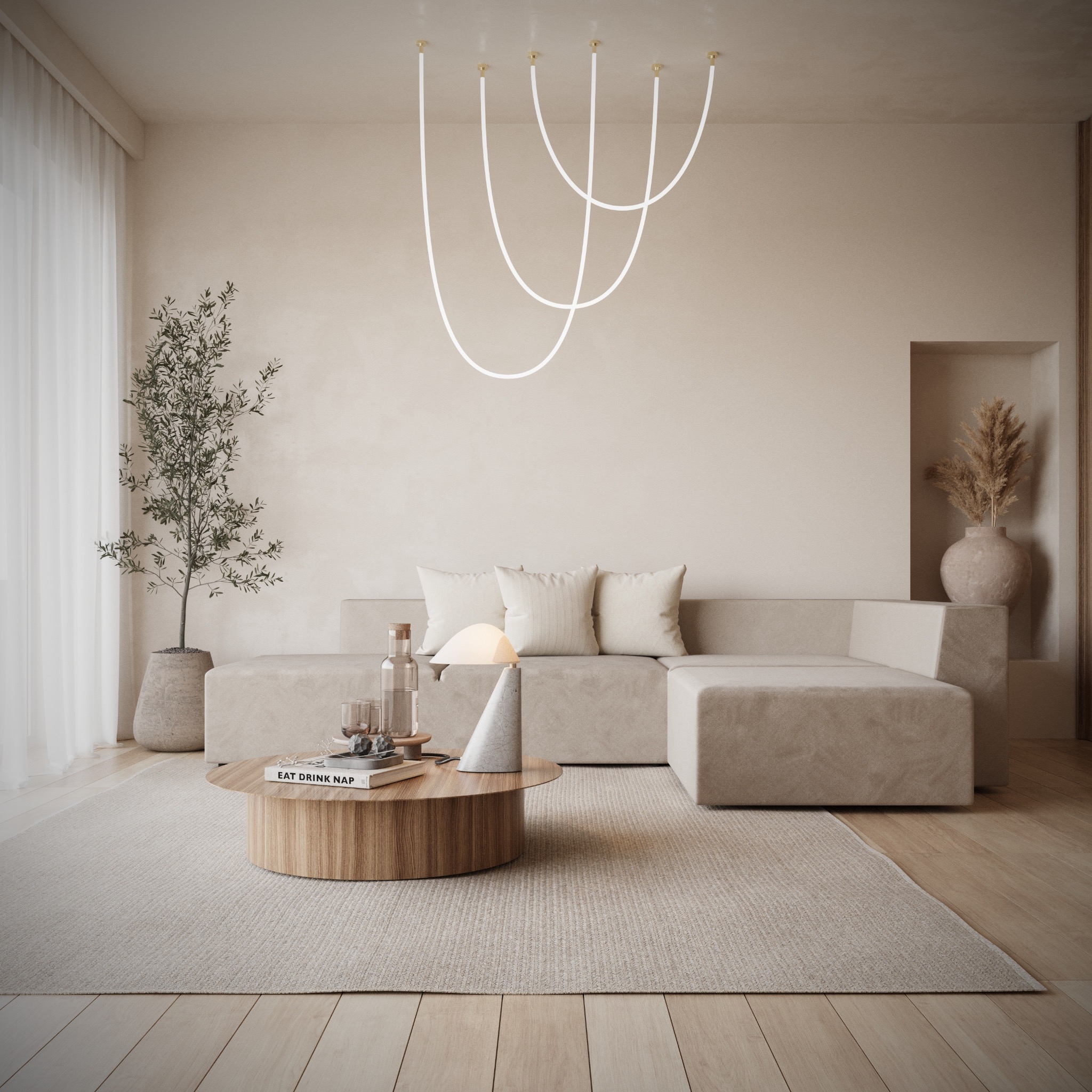 Beżowa sofa modułowa z poduszkami, okrągły stolik kawowy z książką 'Eat Drink Nap', minimalistyczna lampa i podłużna lampa sufitowa w neutralnym salonie z drewnianą podłogą i rośliną w doniczce.