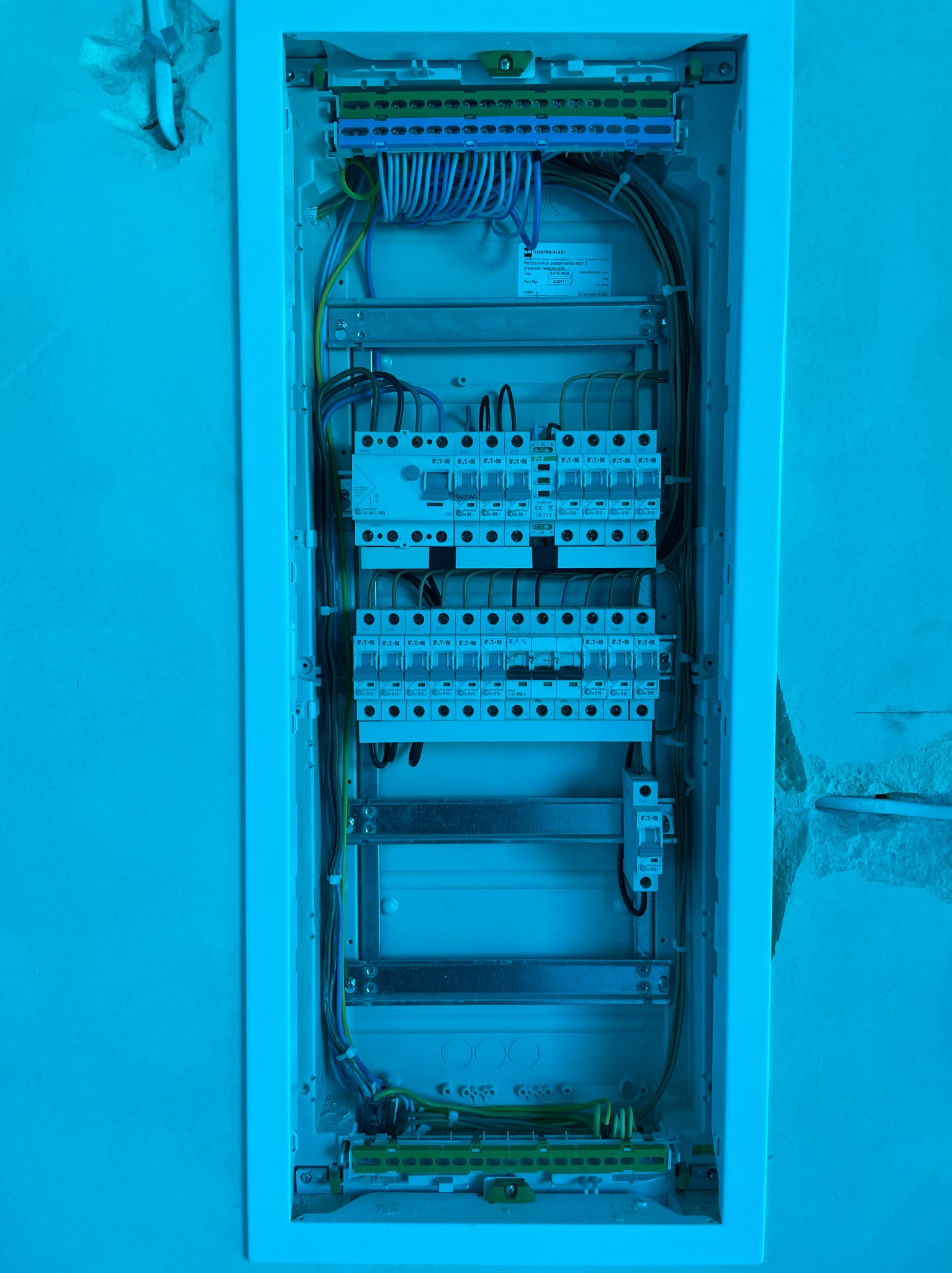 Podtynkowa rozdzielnica elektryczna Eaton z zainstalowanymi bezpiecznikami i okablowaniem, widoczna w surowej ścianie w trakcie montażu.