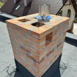 Murowany z cegły komin z metalowym wkładem na dachu budynku w Radomiu, widoczne otwory wentylacyjne w konstrukcji.