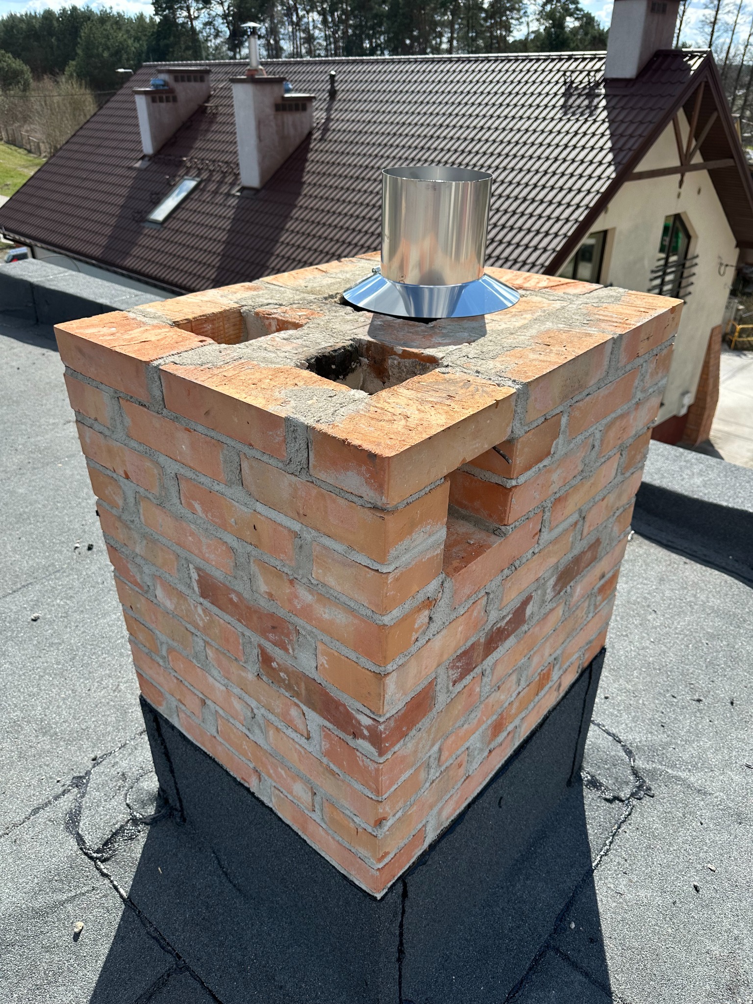 Murowany z cegły komin z metalowym wkładem na dachu budynku w Radomiu, widoczne otwory wentylacyjne w konstrukcji.