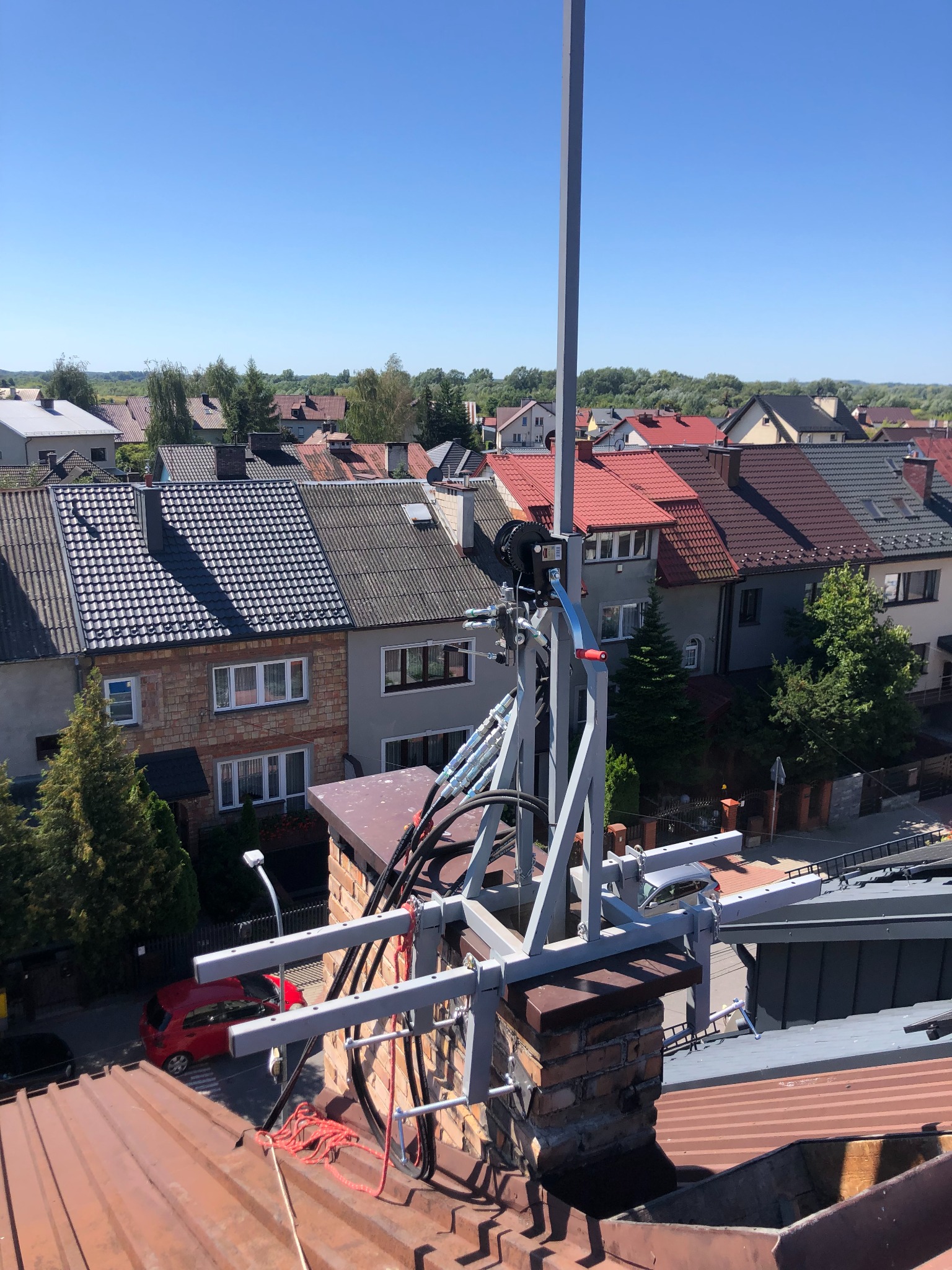 Montaż anteny na kominie z widokiem na zabudowę jednorodzinną w słoneczny dzień.
