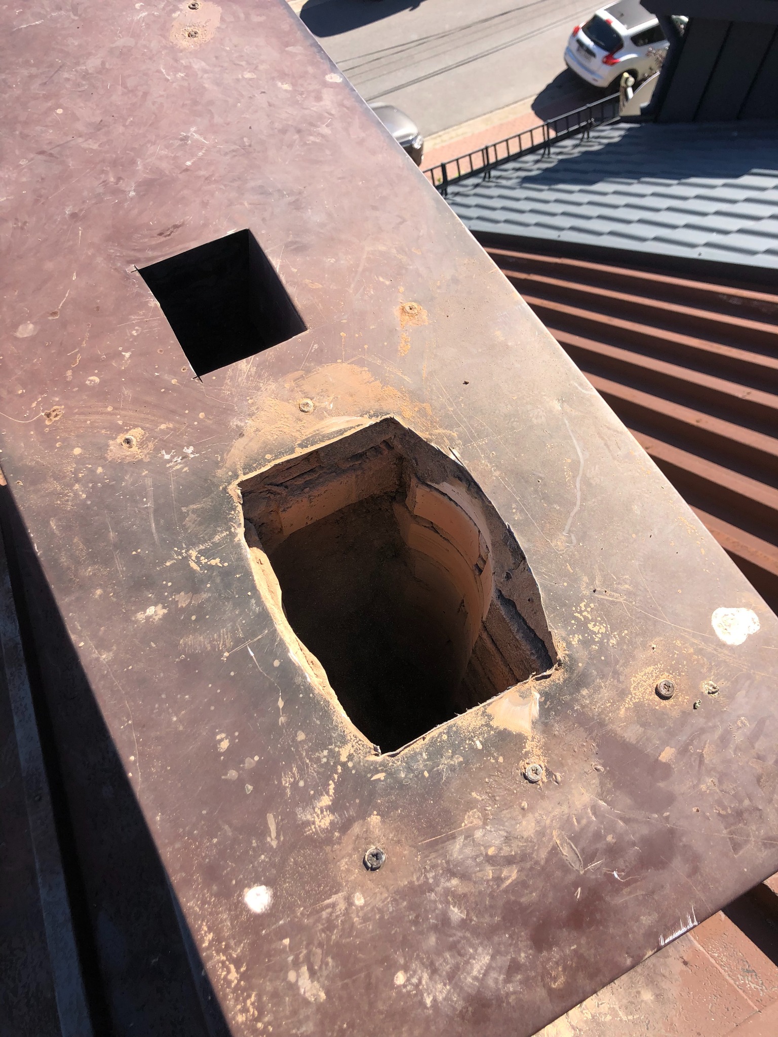 Otwarty przewód kominowy z ceglaną strukturą wewnętrzną, widoczny z góry, z elementami dachu i ulicy w tle.