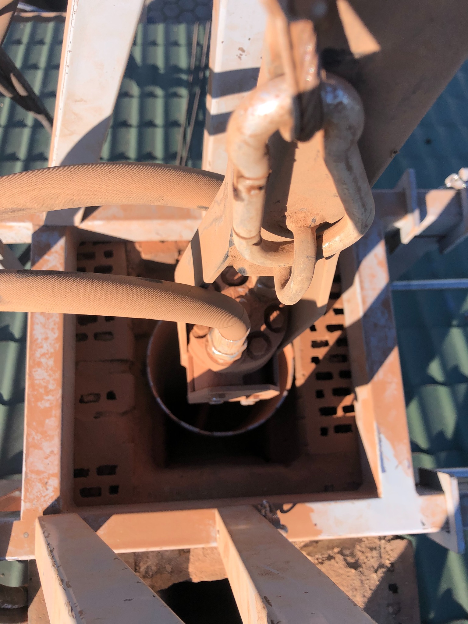 Wnętrze komina z widocznymi elementami konstrukcyjnymi i przewodami, pokryte warstwą rdzawo-brązowego pyłu, na tle zielonego dachu.