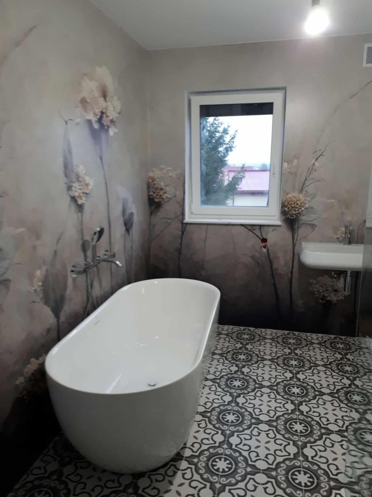 Nowoczesna łazienka z wolnostojącą białą wanną, wzorzystą podłogą i ścianami z motywem kwiatowym, oświetlona górnym światłem.