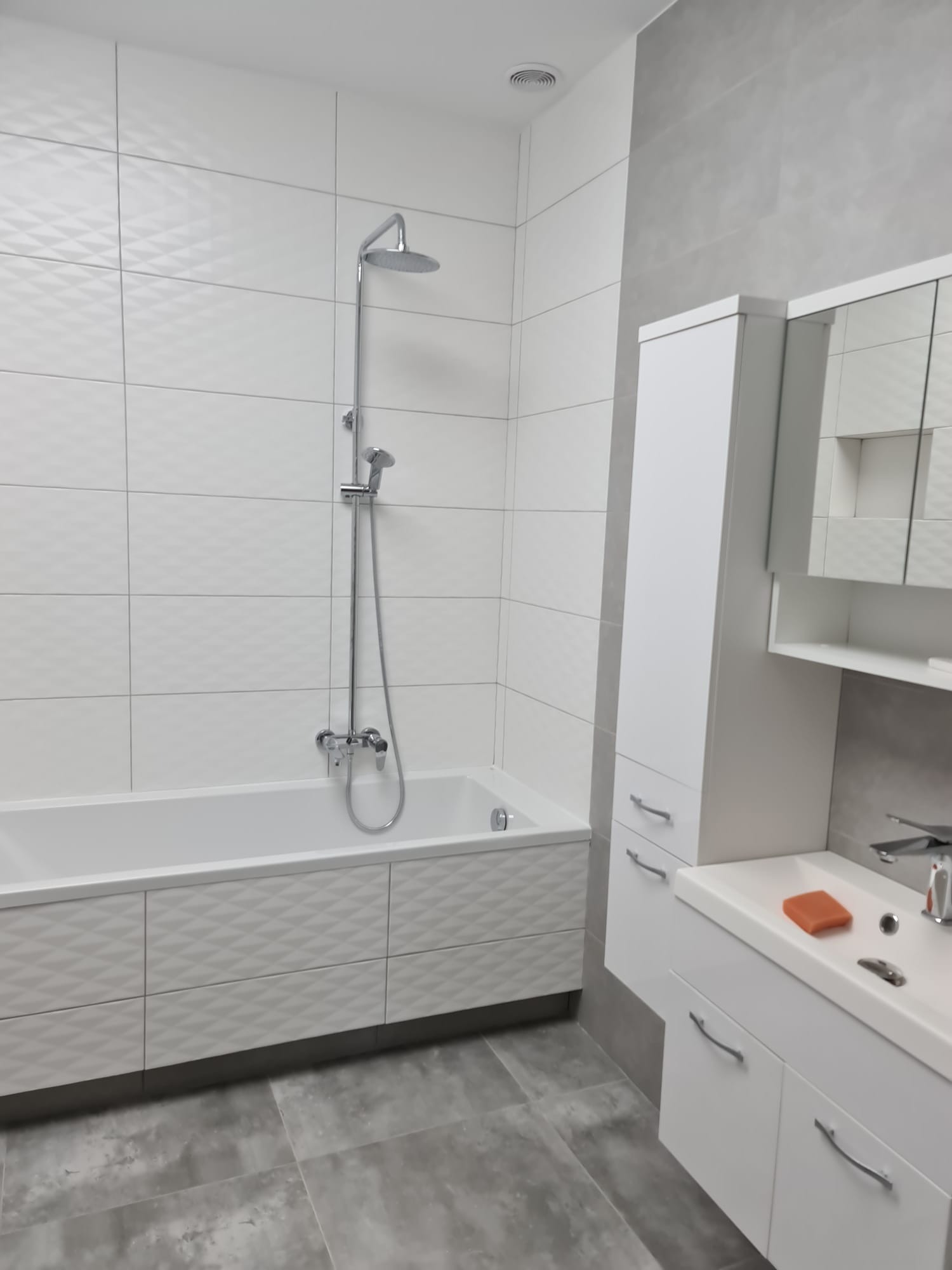 Nowoczesna łazienka w bieli i szarościach: wanna z mozaikową obudową, kabina prysznicowa, umywalka z szafką i lustrem. Minimalistyczny design, gładkie płytki.