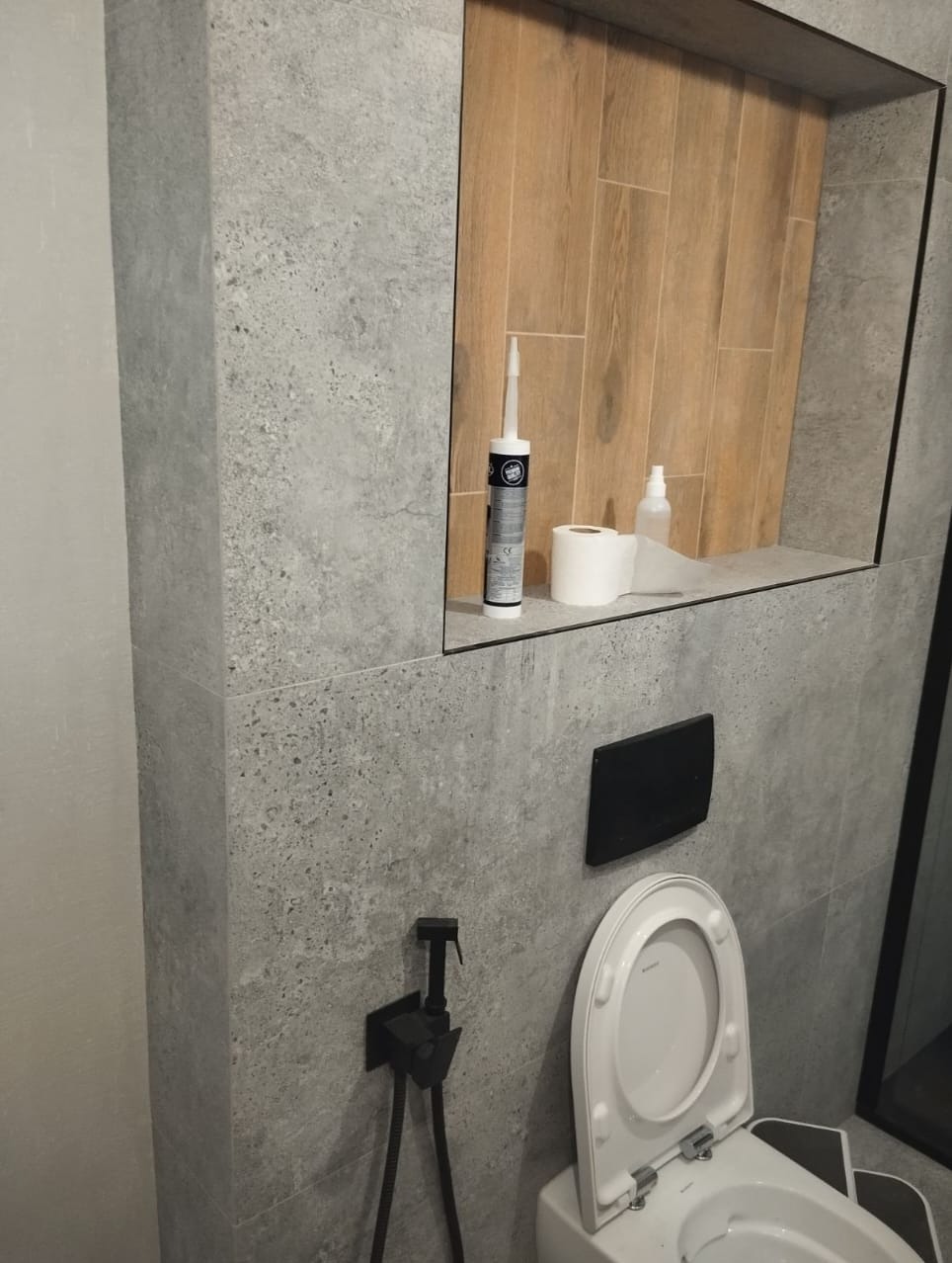 Wykończona łazienka w Pruszkowie: szare płytki imitujące kamień, drewnopodobna wnęka z silikonem, toaleta z bidetką. Nowoczesny design.