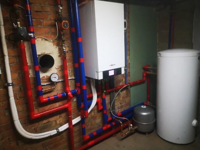 Nowoczesny piec gazowy Viessmann z podłączonym zasobnikiem wody, instalacja z rur w kolorach czerwonym i niebieskim, widoczna ceglana ściana w tle.