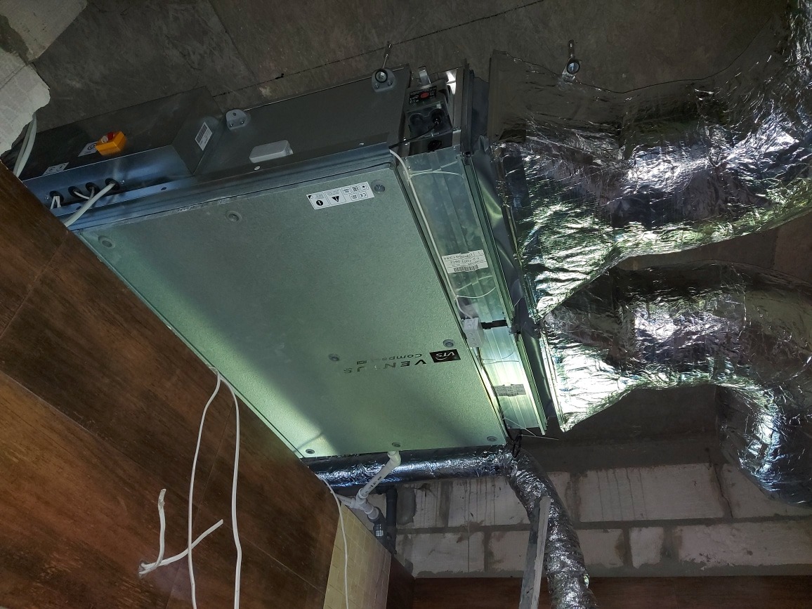 Centrala wentylacyjna z rekuperacją zamontowana pod sufitem, widoczne przewody wentylacyjne w izolacji aluminiowej.