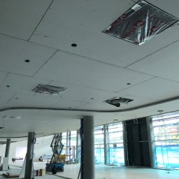 STORO-BUD Oleksandr Storozhenko - Montaż sufitu podwieszanego z płyt kartonowo-gipsowych w dużej przestrzeni biurowej. Widoczne otwory na oświetlenie i elementy instalacji. Prace w toku, widoczny podnośnik.
