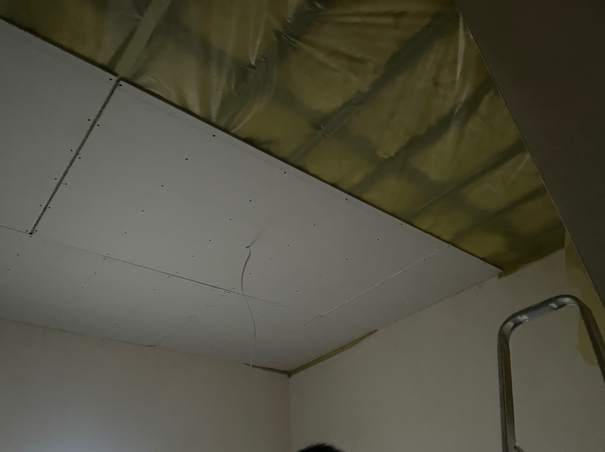 Montaż płyt karton-gips na suficie poddasza, widoczne profile i izolacja. Fragment drabiny w prawym dolnym rogu. Ujęcie z dołu, sufit pod skosem.