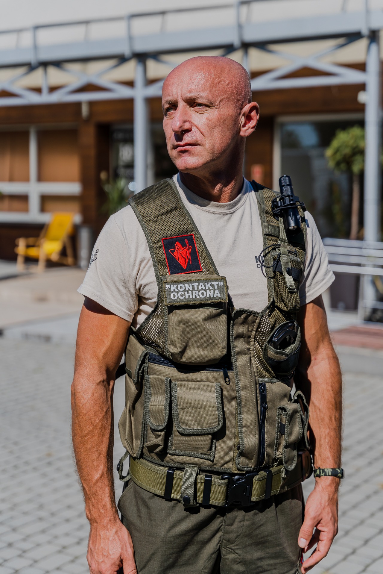 Ochroniarz firmy 'Kontakt Ochrona' w Niepołomicach, w pełnym umundurowaniu, z naszywką firmy, stojący na zewnątrz budynku.