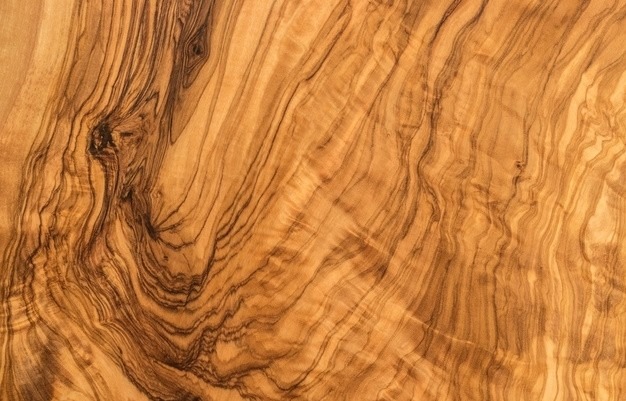 Zbliżenie na naturalny, wzorzysty fornir z drewna oliwnego. Unikalny rysunek słojów w ciepłej, brązowo-żółtej tonacji. Idealne jako wykończenie mebli.