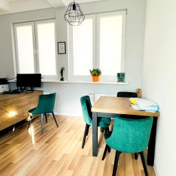 Kancelaria Adwokacka Adwokat Tomasz Siwek - Jasne biuro z drewnianą podłogą, stołem z dokumentami i zielonymi krzesłami, na parapecie figura Temidy i dyplom.