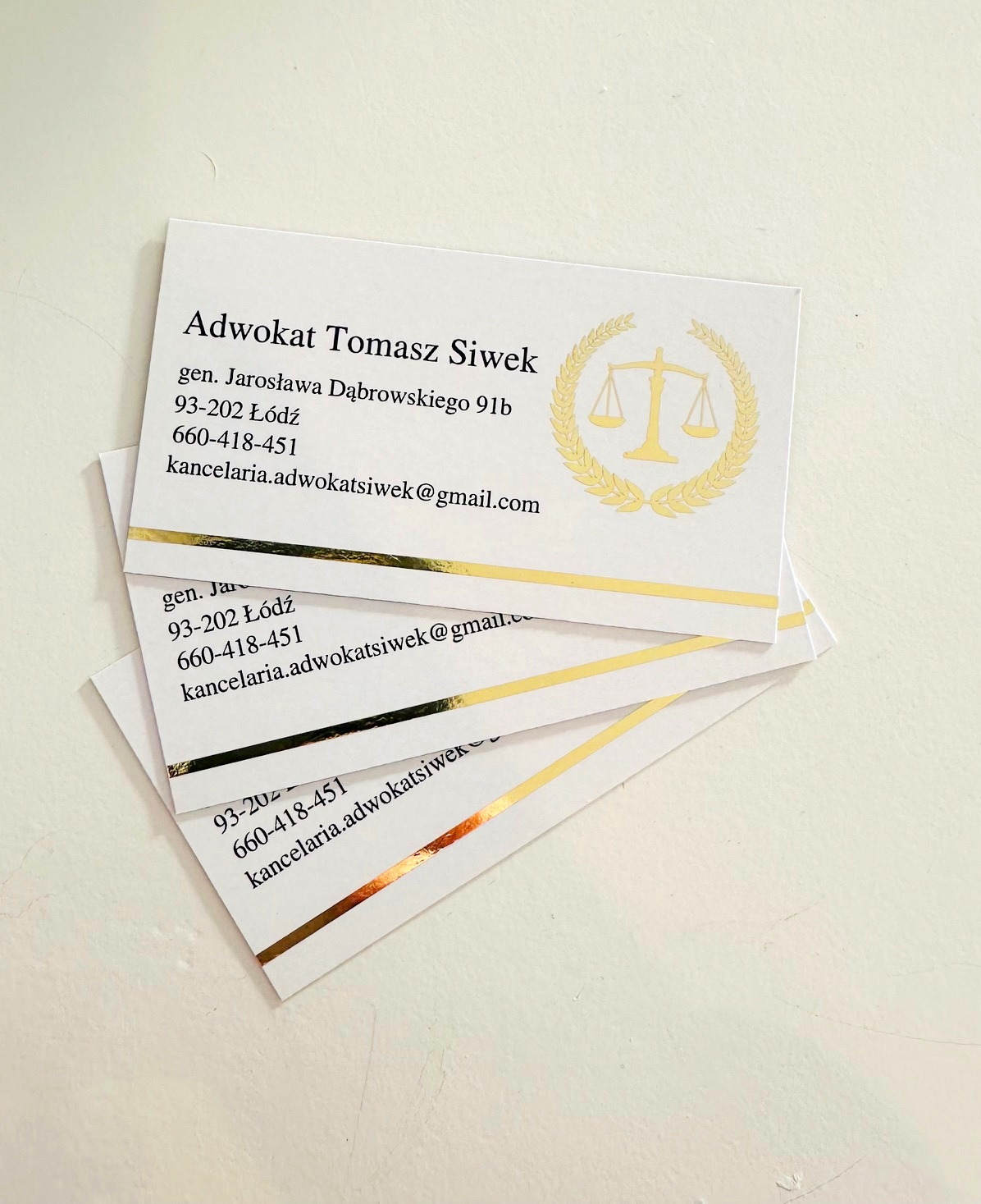 Stos wizytówek Kancelarii Adwokackiej Tomasza Siwka z Łodzi, z adresem, numerem telefonu i adresem e-mail, ozdobionych złotym paskiem i symbolem wagi sprawiedliwości w wieńcu.