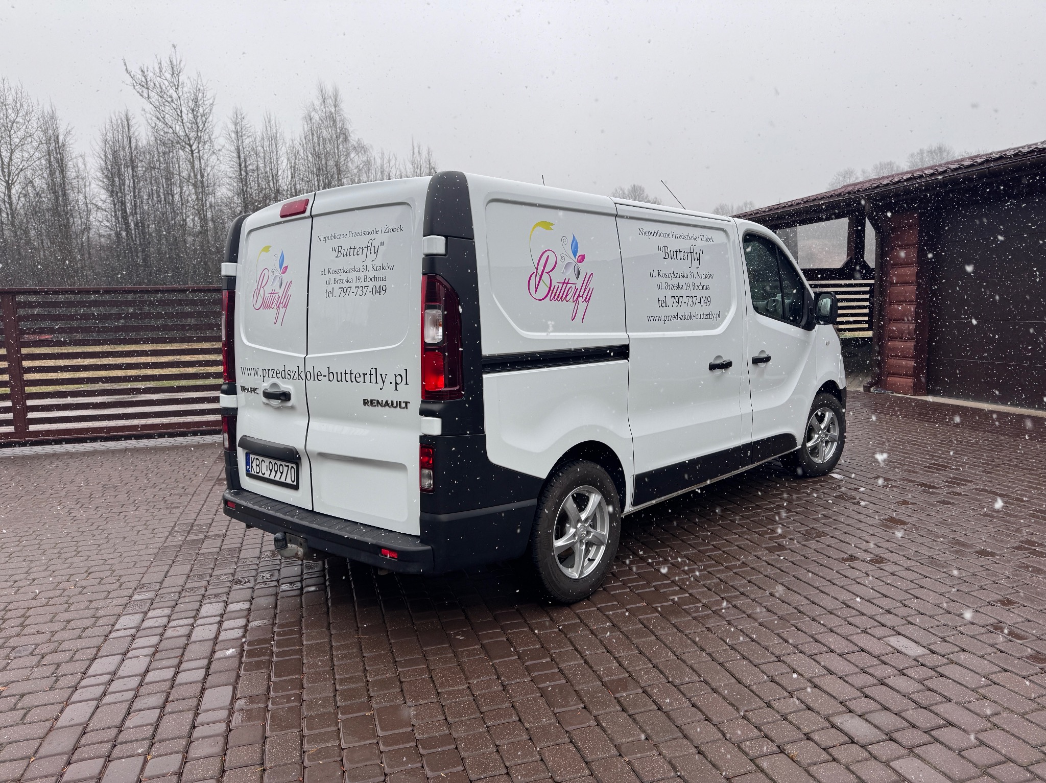 Biały van Renault z oklejeniem Niepublicznego Przedszkola i Żłobka 'Butterfly' na parkingu w zimowy dzień. Widoczny numer rejestracyjny KBC 99970.