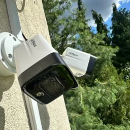 Dwie kamery monitoringu Dahua zamontowane na elewacji budynku, widoczne przewody i elementy montażowe, tło z drzewami i fragmentem nieba.