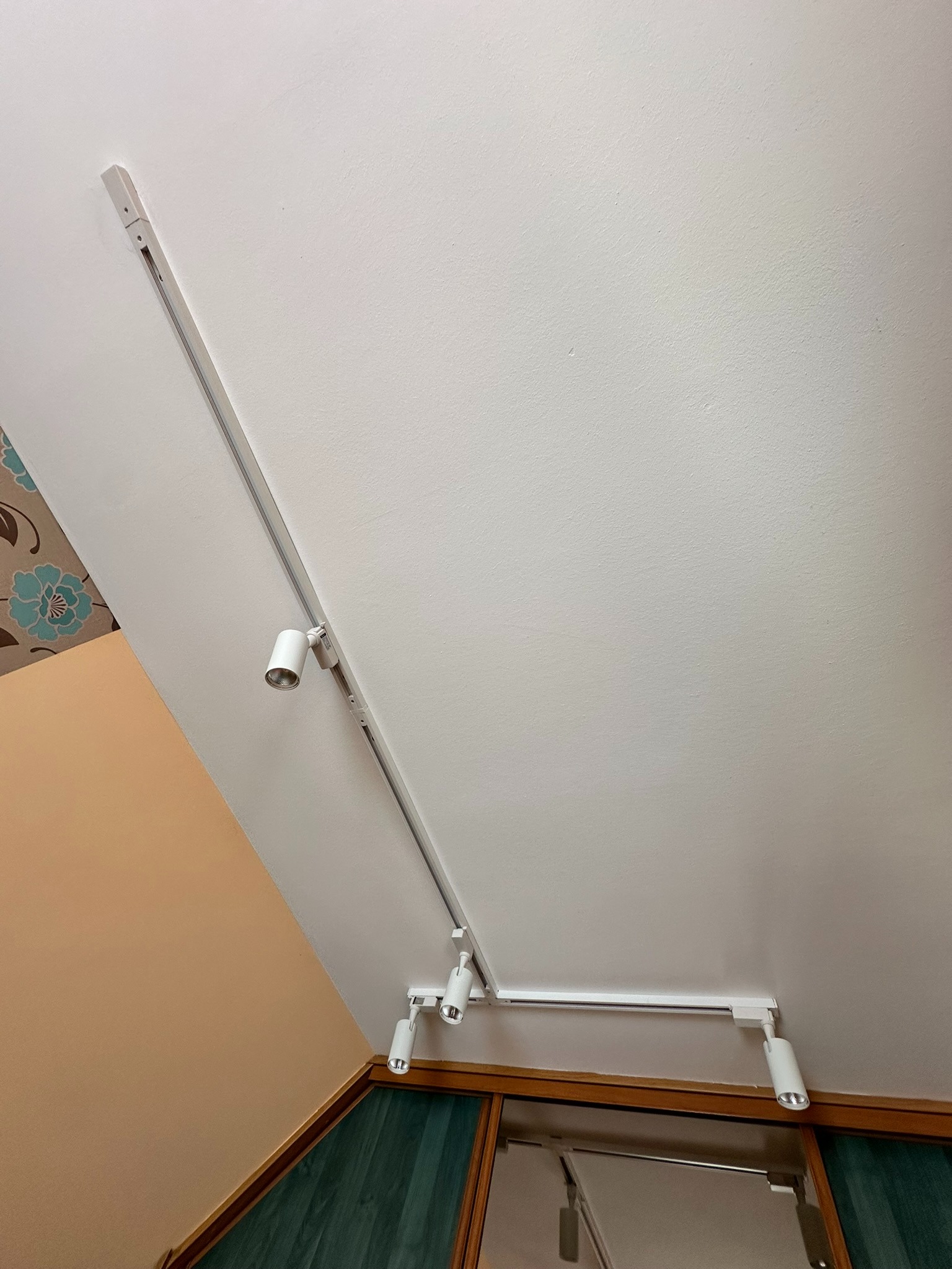 Biały system szynowy z reflektorami punktowymi na skośnym suficie. Widok z dołu ukazuje detale montażu i nowoczesny design oświetlenia.