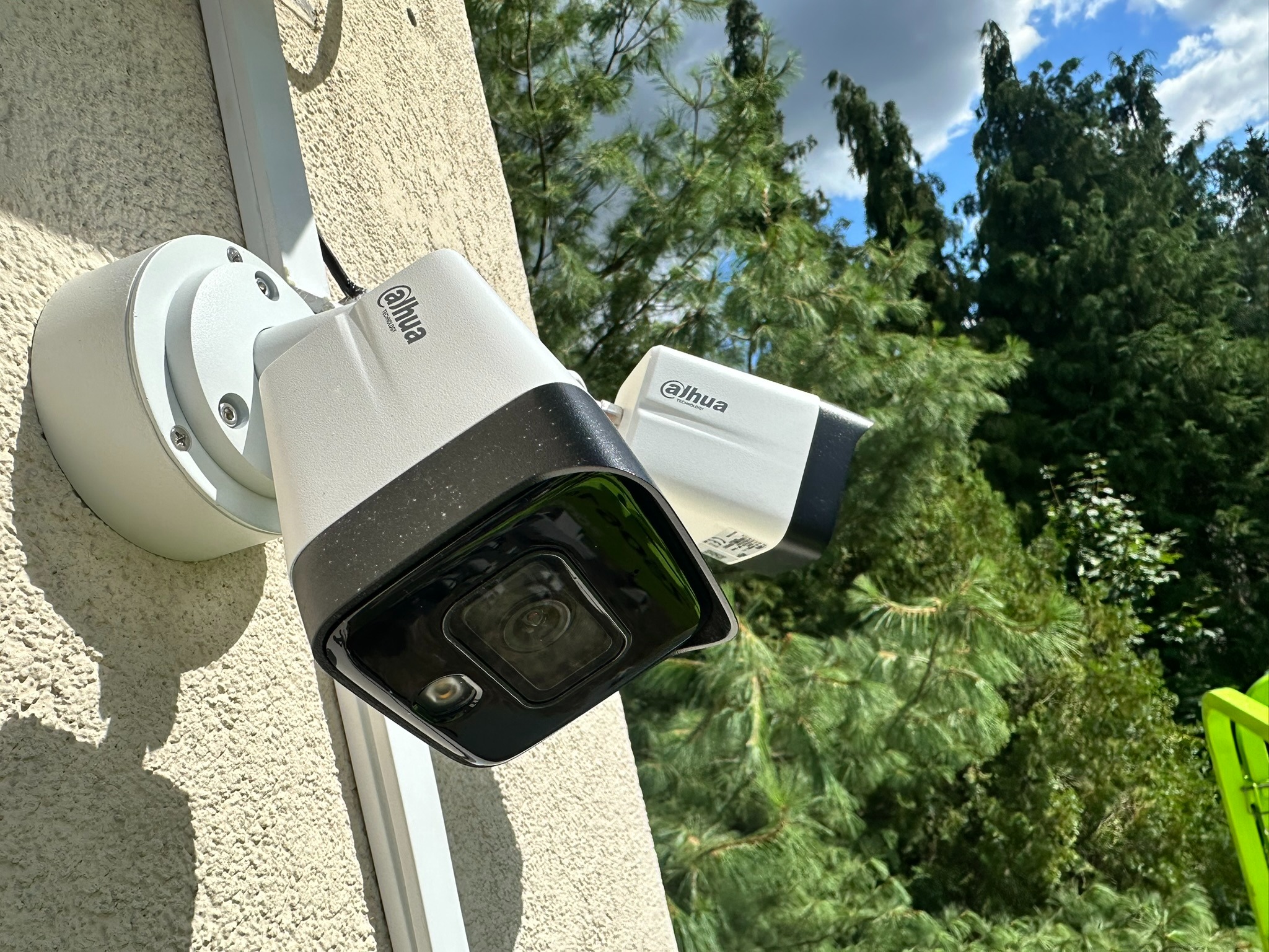 Dwie kamery monitoringu Dahua zamontowane na elewacji budynku, widoczne przewody i elementy montażowe, tło z drzewami i fragmentem nieba.