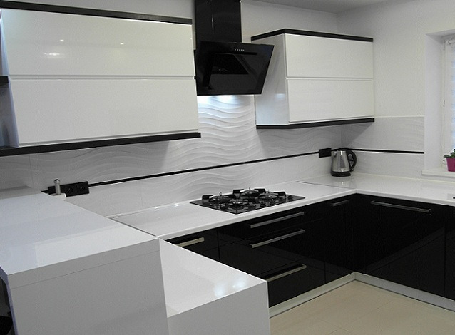 Nowoczesna kuchnia w czarno-białej kolorystyce z błyszczącymi frontami, falistymi płytkami na ścianie i czarnym okapem nad płytą gazową.