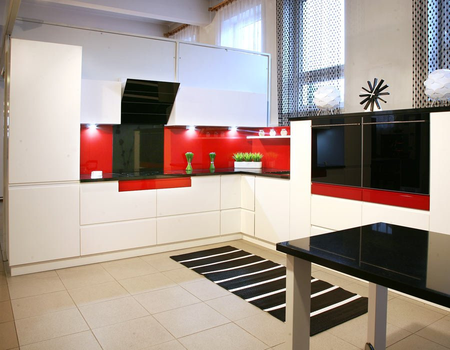 Nowoczesna kuchnia z białymi szafkami, czerwonym panelem szklanym i czarnym okapem, uzupełniona czarno-białym dywanem w paski.