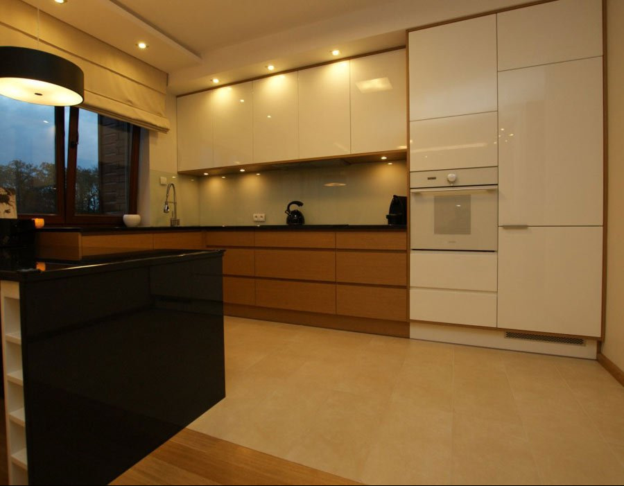 Nowoczesna kuchnia z białymi, lakierowanymi szafkami górnymi i drewnianymi szafkami dolnymi, czarny blat i wyspa kuchenna, oświetlenie punktowe i okno z roletą rzymską.