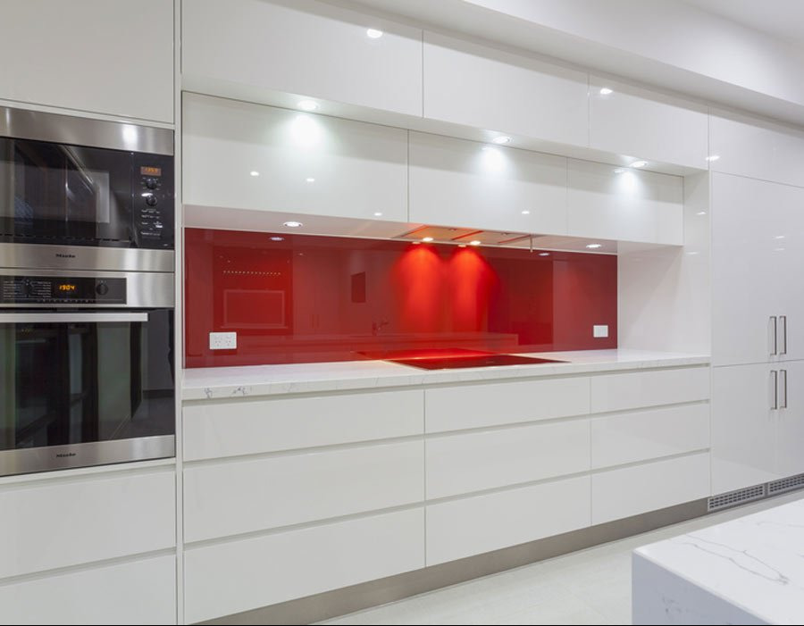 Nowoczesna, biała kuchnia na wymiar z czerwonym panelem szklanym nad blatem, z piekarnikiem i mikrofalówką Miele w zabudowie, zrealizowana w miejscowości Brody.