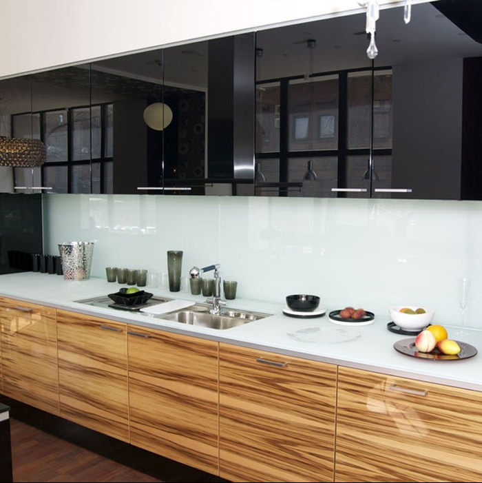 Nowoczesna kuchnia z frontami z egzotycznego drewna zebrano, białym blatem i czarnymi, lustrzanymi szafkami wiszącymi, uzupełniona o szklany panel ścienny i designerskie akcesoria.