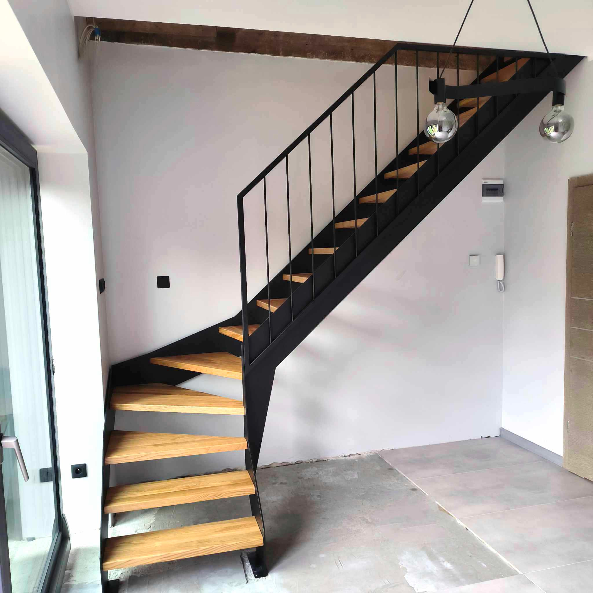 Nowoczesne schody metalowe z drewnianymi stopniami, czarna konstrukcja, minimalistyczny design, widok z dołu, surowe wnętrze w trakcie wykończenia.