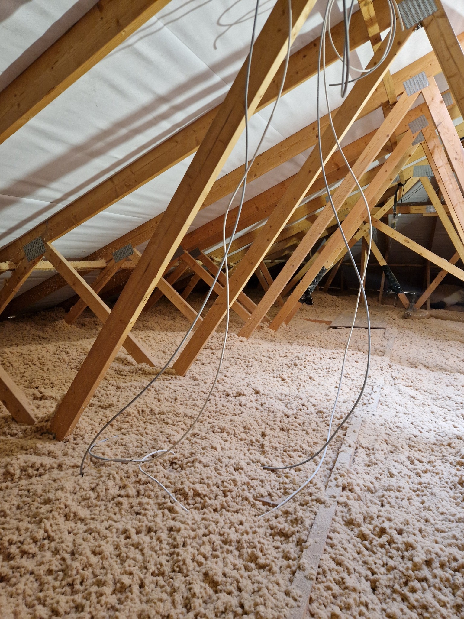 Poddasze z widoczną konstrukcją drewnianą i izolacją z wełny mineralnej, zwisające kable elektryczne.