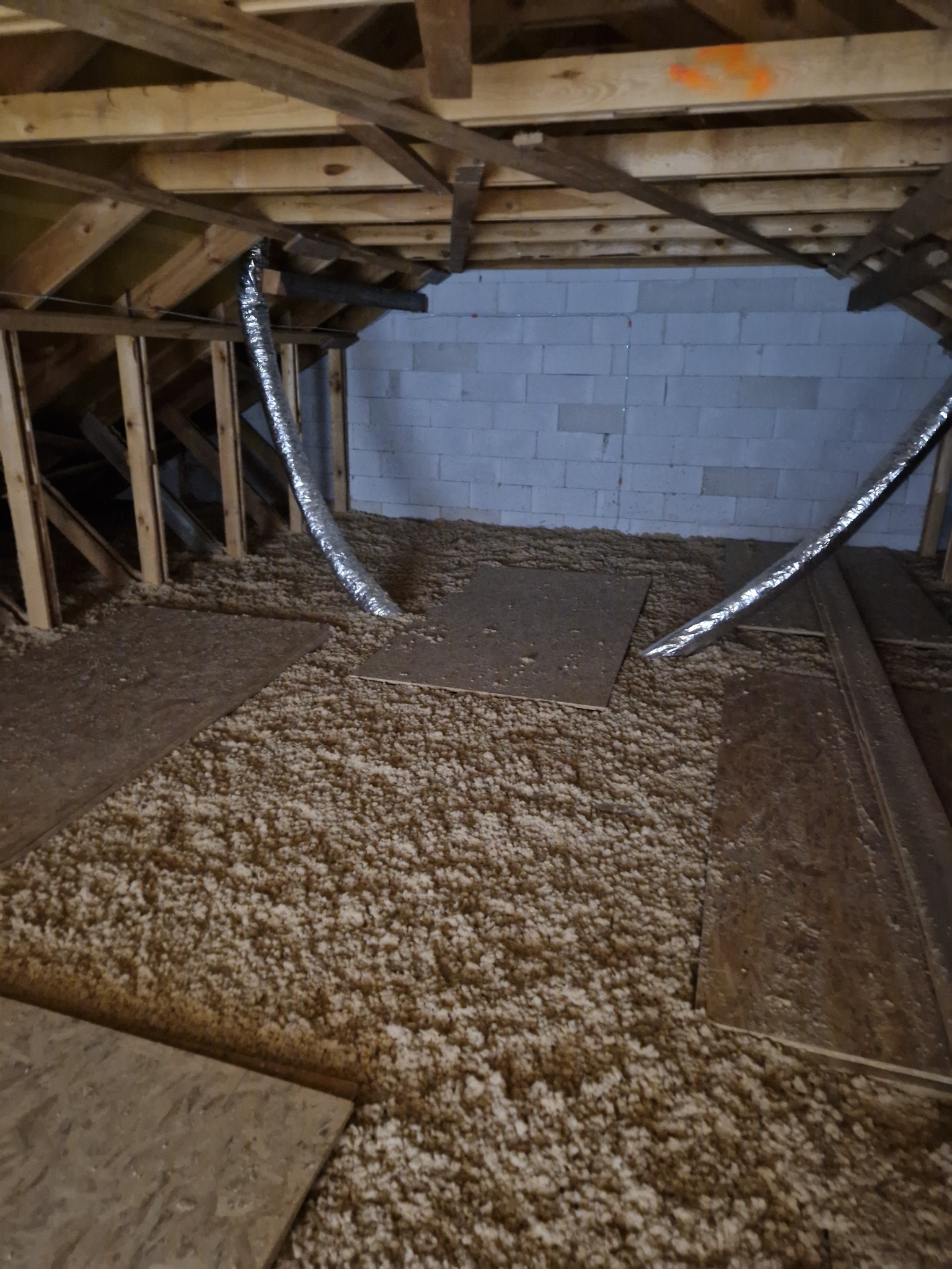 Poddasze z drewnianą konstrukcją i częściowo ułożoną warstwą izolacyjną z wełny mineralnej, widoczne fragmenty płyt OSB i rury wentylacyjne.