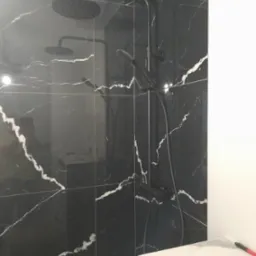 Wykończona kabina prysznicowa z czarnymi płytkami imitującymi marmur i czarną armaturą, widoczne narzędzia na blacie obok.