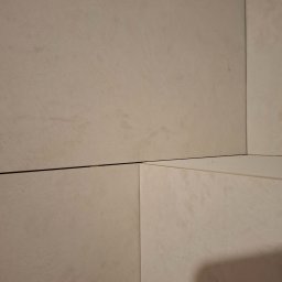 Krzysztof Danowski - Beżowe, matowe płytki ceramiczne ułożone na ścianie, widoczne fugi. Minimalistyczny detal wykończenia wnętrza, kąt ujęcia podkreśla fakturę i łączenia płytek.