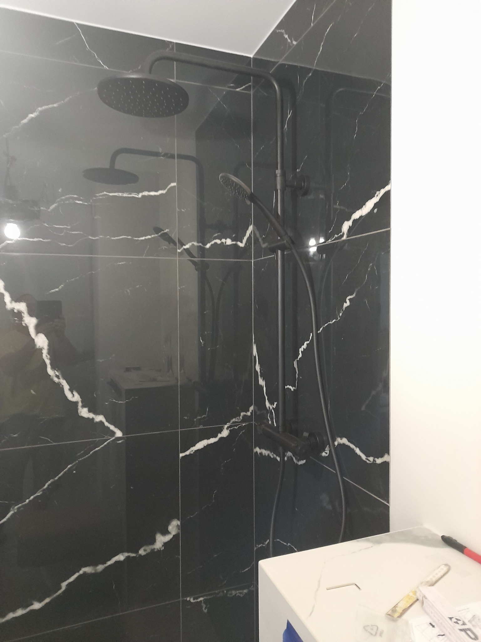 Wykończona kabina prysznicowa z czarnymi płytkami imitującymi marmur i czarną armaturą, widoczne narzędzia na blacie obok.