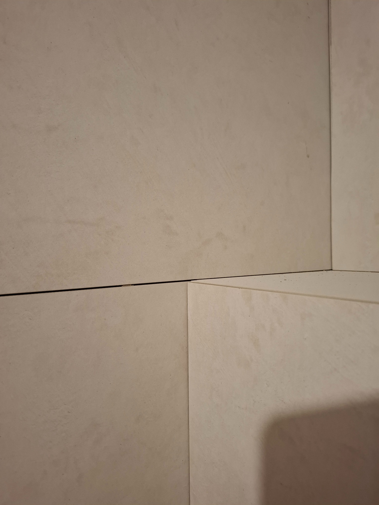 Beżowe, matowe płytki ceramiczne ułożone na ścianie, widoczne fugi. Minimalistyczny detal wykończenia wnętrza, kąt ujęcia podkreśla fakturę i łączenia płytek.