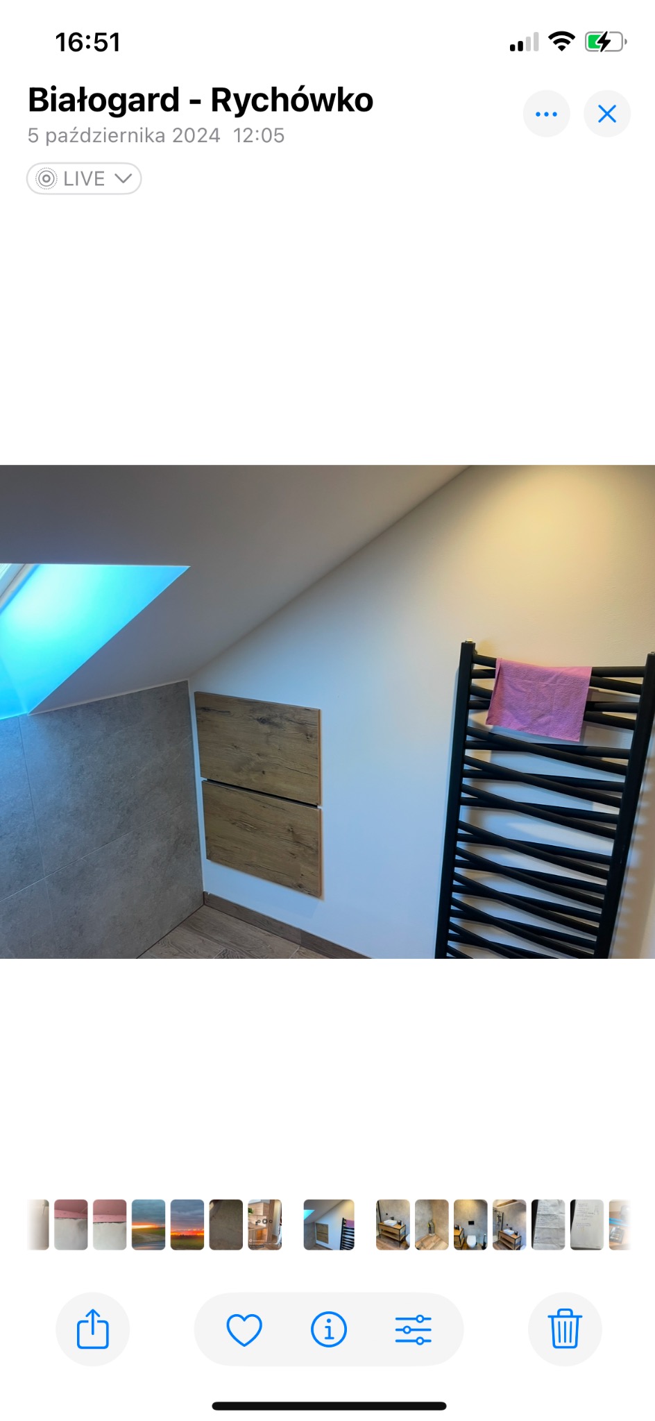 Wykończona łazienka na poddaszu z oknem dachowym, szarą płytką, zabudową meblową z drewnianymi frontami i czarnym grzejnikiem drabinkowym z różowym ręcznikiem.