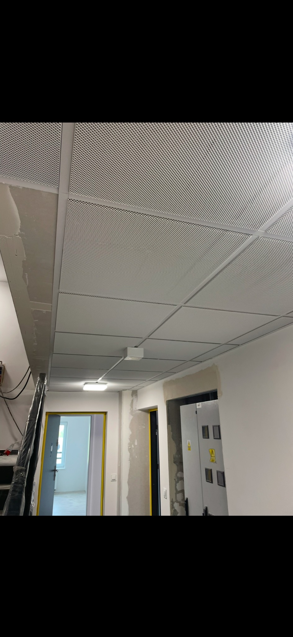 Montaż sufitu podwieszanego rastrowego w biurze, widoczne kable i oświetlenie, ściany przygotowane do malowania.