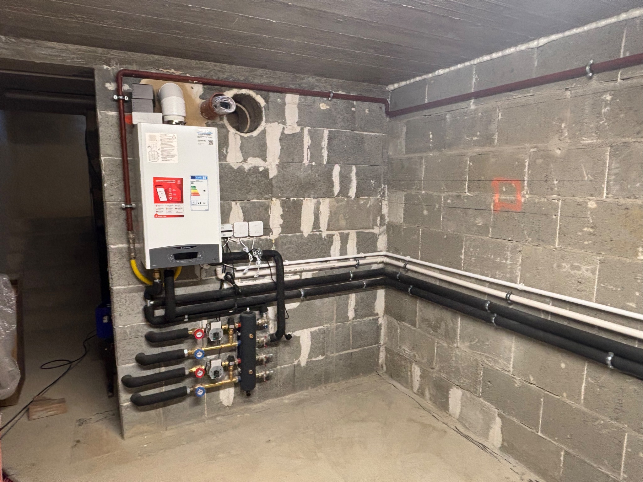 Zrealizowana instalacja CO w piwnicy: nowy piec gazowy, rury grzewcze z izolacją, zawory i sterowniki na szarej ścianie z betonu komórkowego. Instalacja schludna, estetyczna.